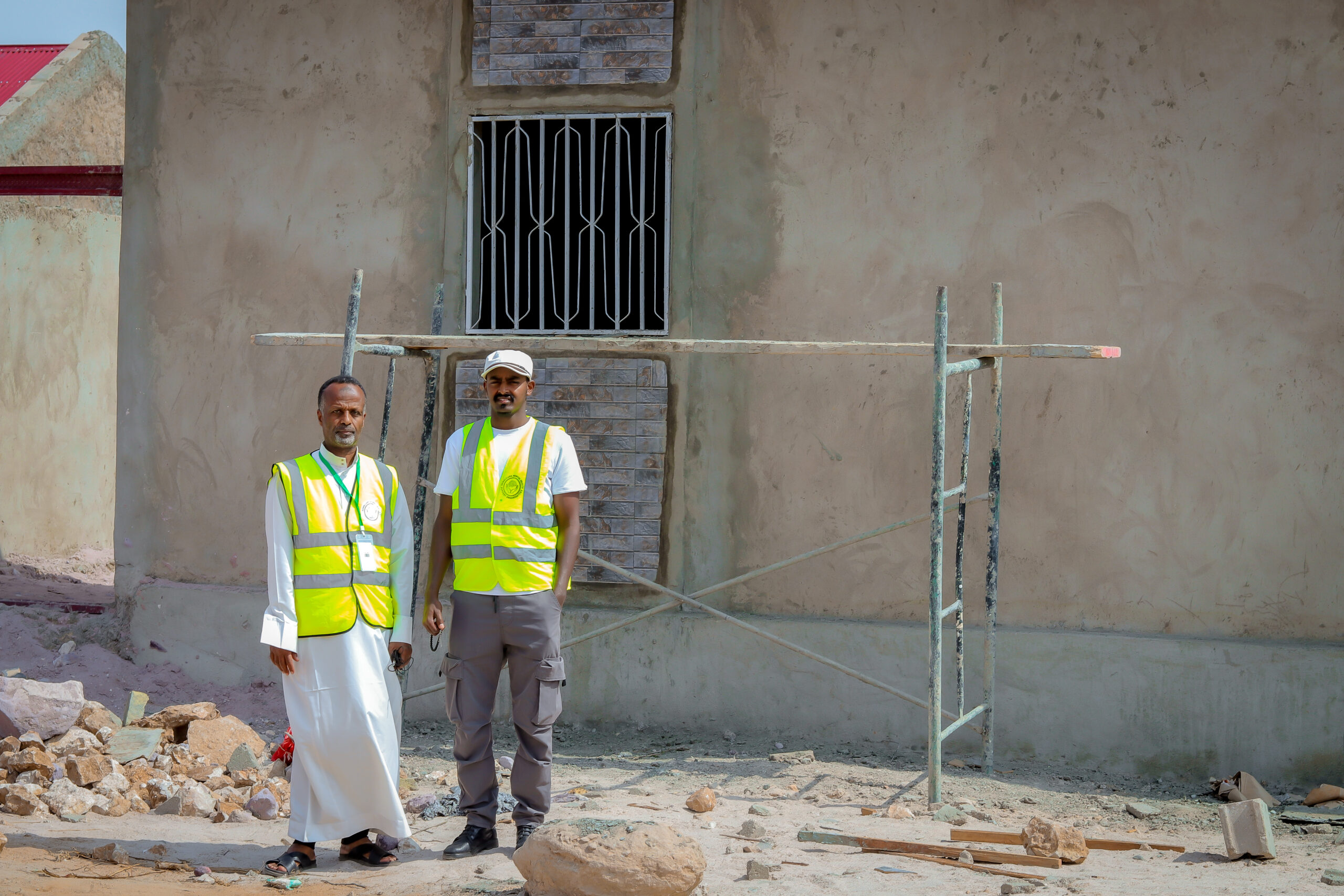 Two people in high-visibility vests standing in front of a building under construction.
