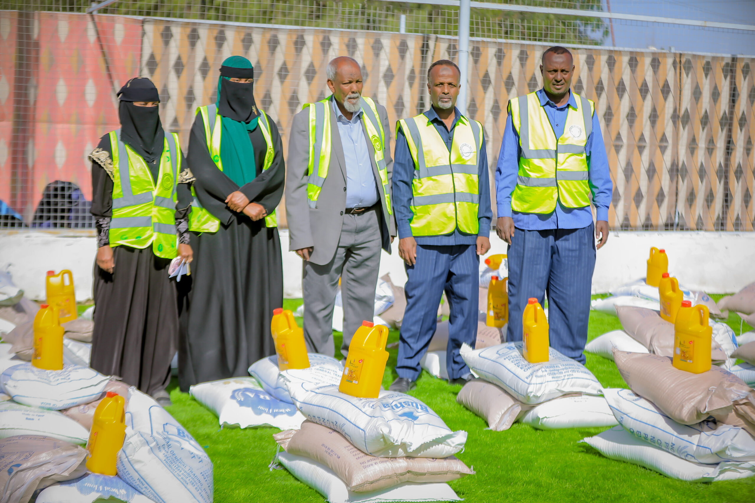 Five people in high-visibility vests standing beside bags of food and bottles of oil.